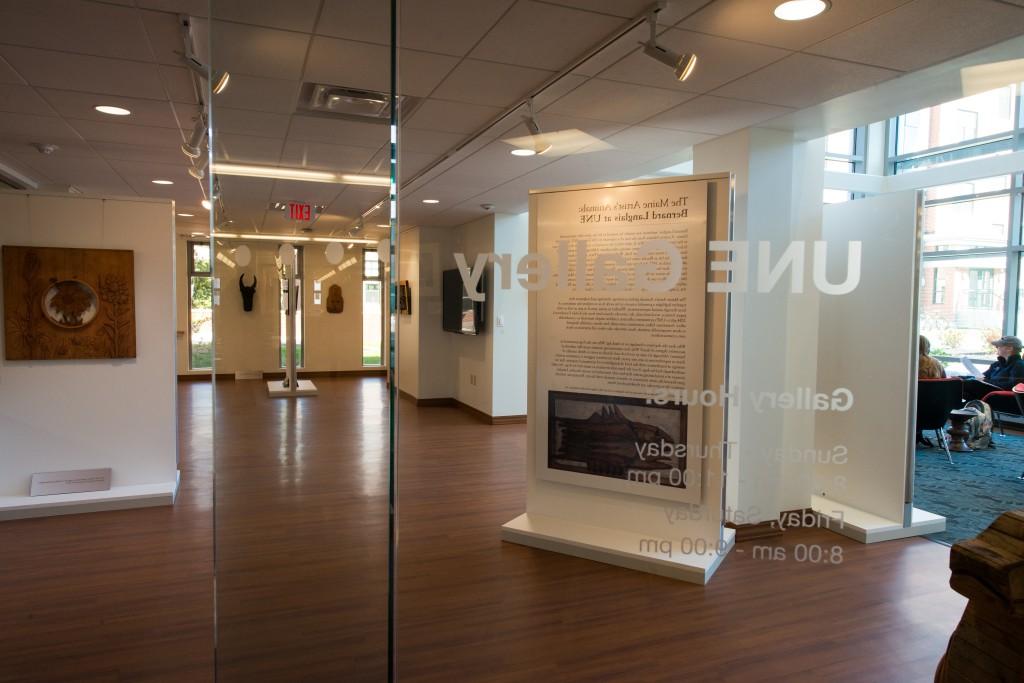 An interior shot of the art gallery on the Biddeford Campus featuring a glass door that says "U N E Gallery." Artwork hanging inside can be seen through the door.