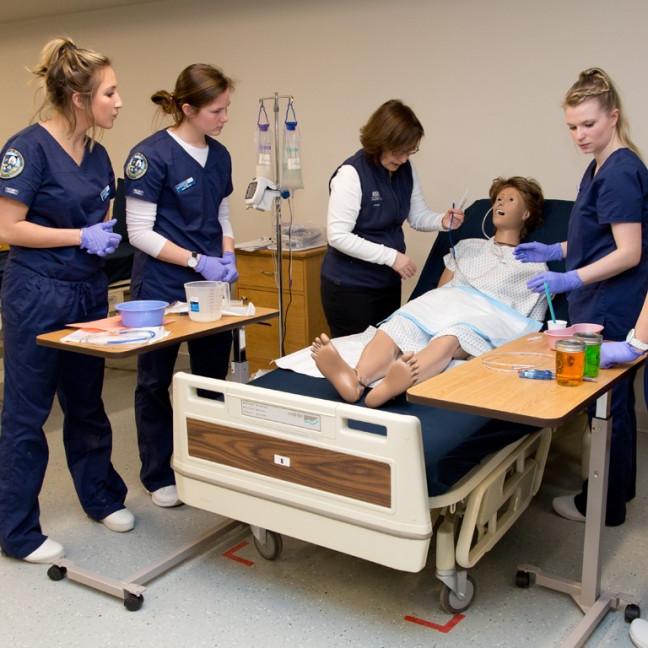 three students and a professor work on a patient simulator